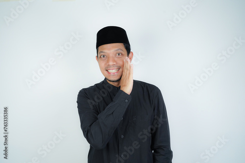 Asian Muslim man telling secrets in mouth, whispering gossip, wearing Arab turban sorban at copy space on isolated background photo