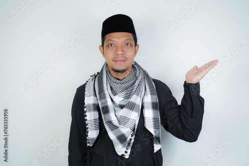 Cheerful handsome Asian Muslim man wearing Arab turban sorban pointing hand finger at empty space for advertising on isolated background photo