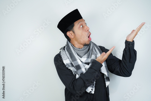 Wow face shocked expression Asian Muslim man wearing Arab turban sorban pointing hand finger at empty space on isolated background photo