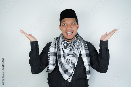 Cheerful handsome Asian Muslim man wearing Arab turban sorban pointing hand finger at empty space for advertising on isolated background photo