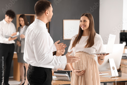 Young pregnant businesswoman working with her colleague in office
