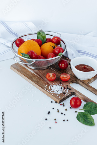 red cherry tomatoes on branches and yellow tomatoes in a colander with basil leaves, on a wooden board with coarse salt and pepper, tomato halves on a white background.white towel,a bowl of ketchup
