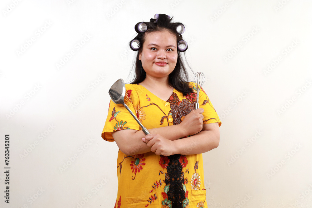 Happy asian housewife standing while holding cooking tools. Isolated on white Happy asian housewife standing while holding cooking tools. Isolated on white