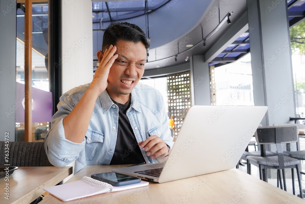 Asian man get pressure Tired headache, having Neck Pain, using laptop, mobile phone in coffee shop, online business Asian man get pressure Tired headache, having Neck Pain, using laptop, mobile phone in coffee shop, online business