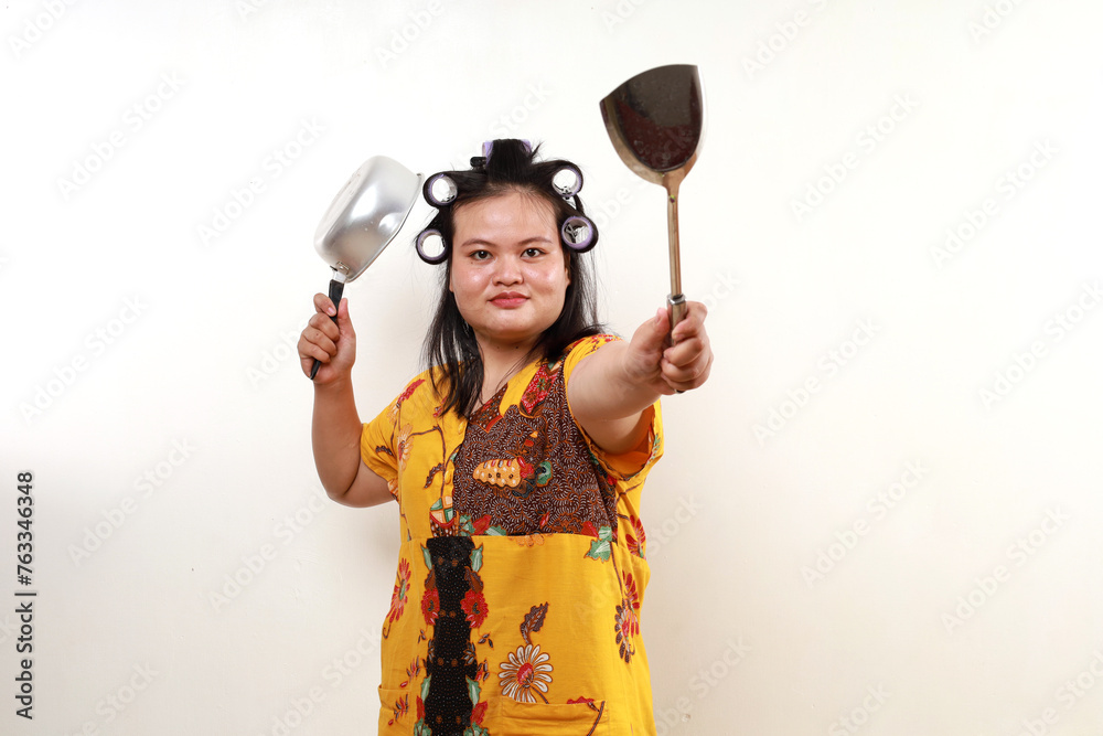 Happy asian housewife standing while holding cooking tools. Isolated on white Happy asian housewife standing while holding cooking tools. Isolated on white