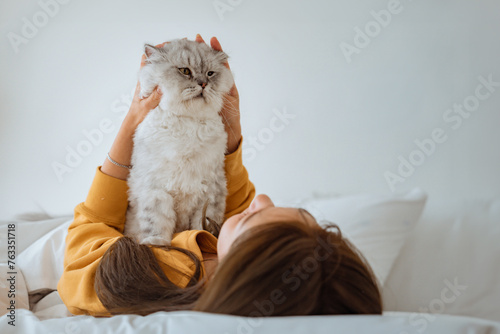 Happy asian woman massages with fluffy grey cat with relax on the bed at home, A touching moment between a pet and its owner, Friendship with pets