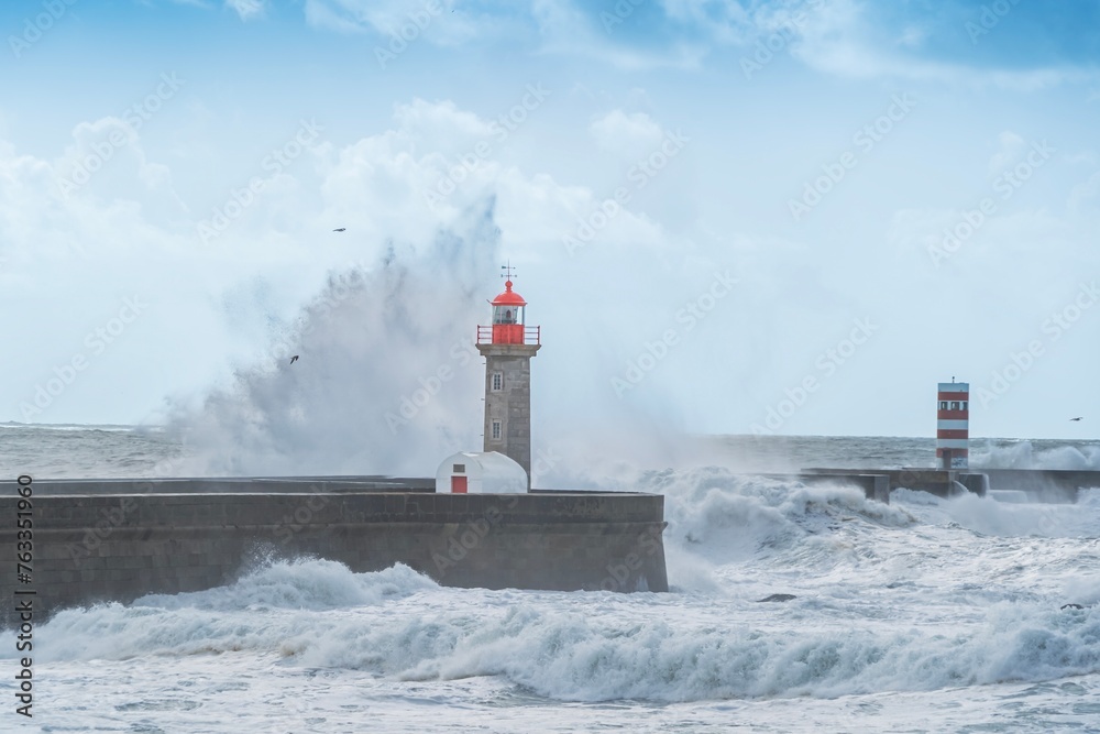 Storm waves over lighthouse, Portugal - sky enhanced. Windy coast. Bad weather with waves crashing in Porto harbor.