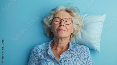 Elderly woman sleeping on pillow isolated on pastel blue colored background Sleep deeply peacefully rest. Top above high angle view photo portrait of satisfied .senior wear blue shirt photo