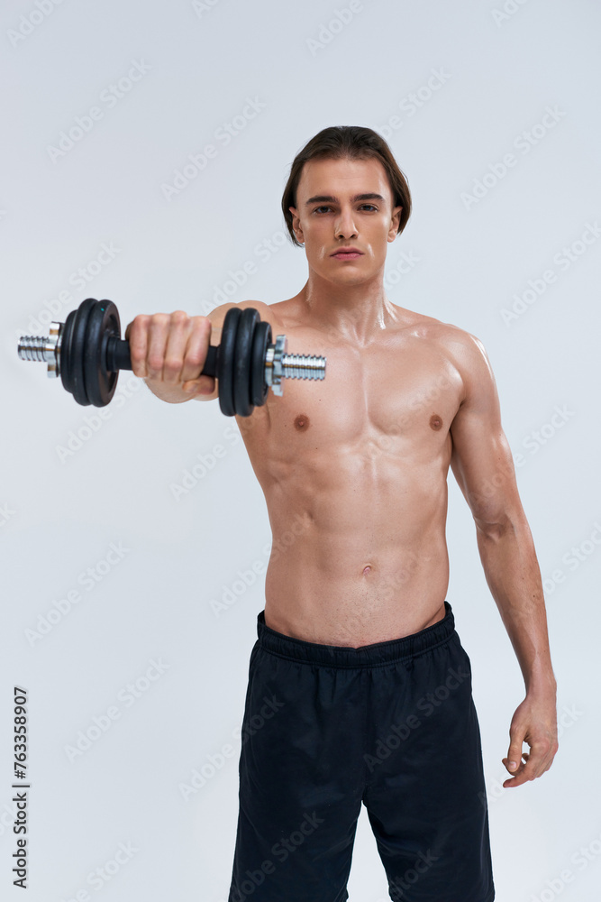 attractive athletic man posing topless exercising actively with dumbbell and looking at camera