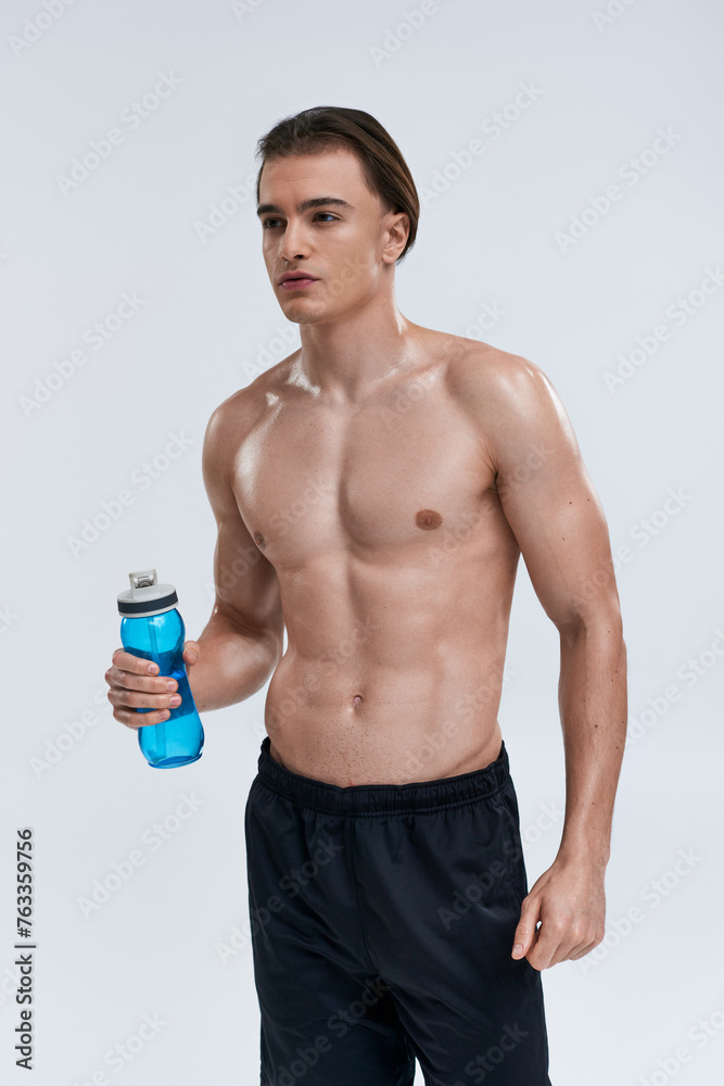 handsome sexy male model in black pants holding water bottle and looking away on gray backdrop handsome sexy male model in black pants holding water bottle and looking away on gray backdrop