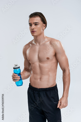handsome sexy male model in black pants holding water bottle and looking away on gray backdrop