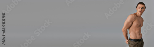 sexy shirtless man in brown pants posing attractively on gray backdrop and looking away, banner