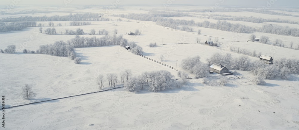 A snow-covered rural field with a house and trees from an aerial perspective
