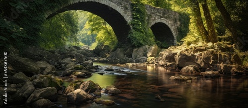 A stone bridge crossing a river with boulders in the foreground