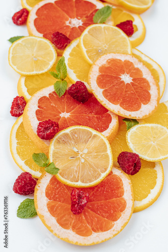 slices of orange, lemon and grapefruit, mint leaves and raspberries on a white background