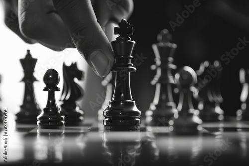 A black and white photo of a chess board with a hand reaching for the king