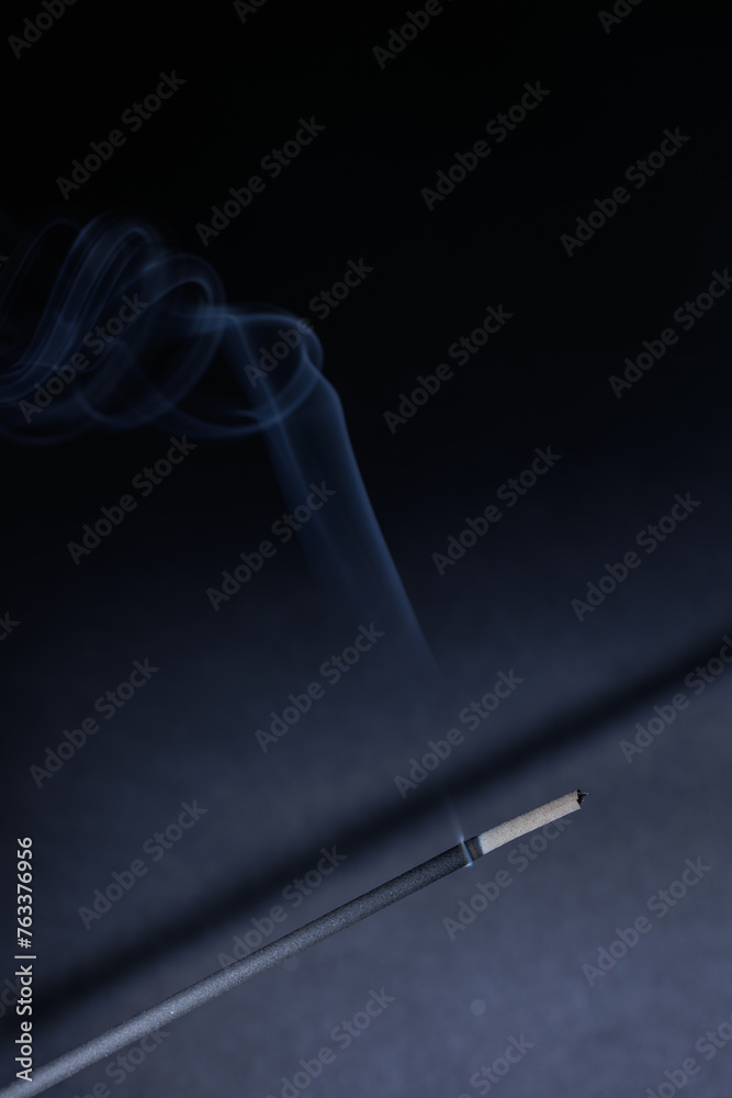 A closeup of incense stick and a knee shaped fume on the black textured background for graphic and web design use A closeup of incense stick and a knee shaped fume on the black textured background for graphic and web design use