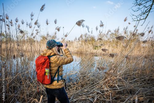 Woman naturalist is watching birds with binoculars. Observation wildlife animals at lake photo