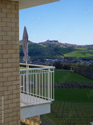 Scenic view from a balcony with a closed sun umbrella, of green hills, vineyards and the town of Fermo in the background; Monte Urano, Marche, Italy photo