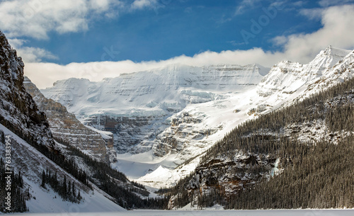 Scenic view of snow covered mountains and glacier with blue sky and clouds overshadowing the snow covered lake; Lake Louise, Alberta, Canada photo