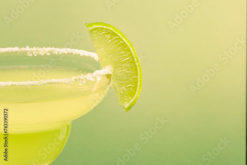 Close up of a lime wedge on salt rim of margarita glass isolated on pale green pastel color background with room for text.