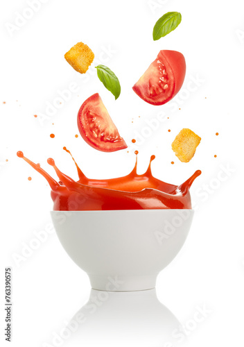 Tomato, croutons and basil leaves falling into a splashing bowl of soup isolated on white background.