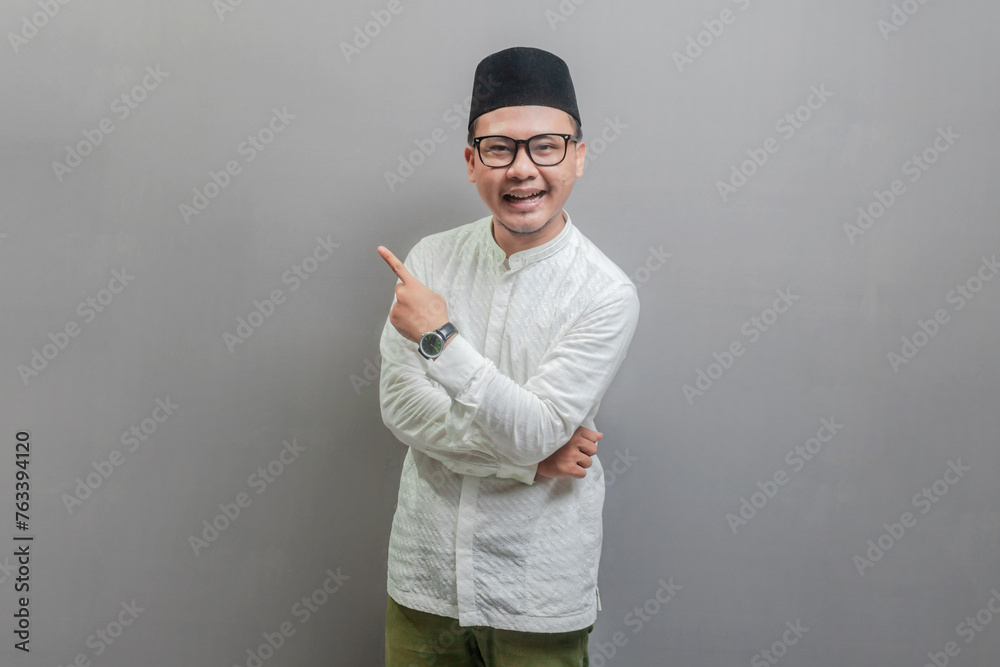 Asian Muslim man standing looking camera and pointing finger to right empty space Asian Muslim man standing looking camera and pointing finger to right empty space