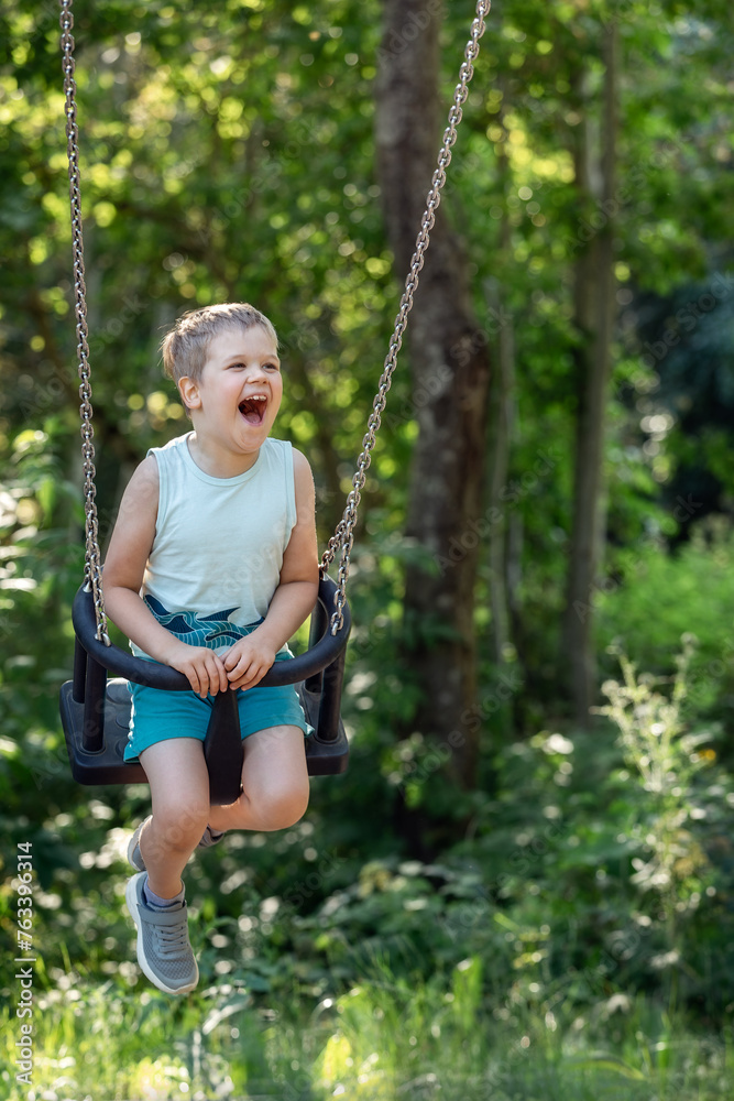 A very cheerfully laughing child swings on long chain swings against the background of nature.