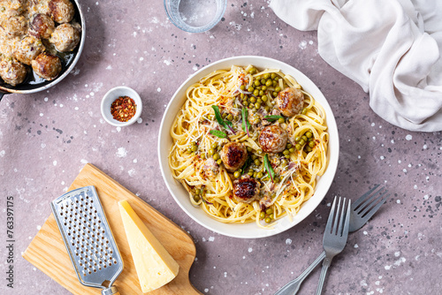 Spaghetti with meatballs and cream sauce is served on a plate with herbs and parmesan.