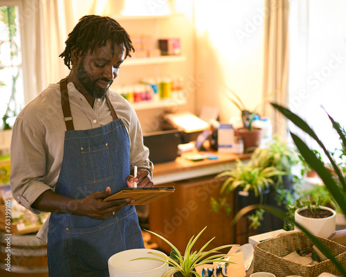 Man Working In Sustainable Plastic Free Grocery Store Checks Stock On Shelves With Digital Tablet photo