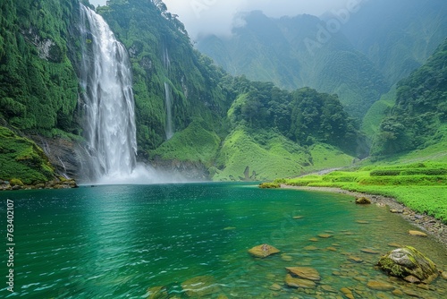 A dense jungle encloses a tall waterfall  shrouded in mist and vibrant green foliage.