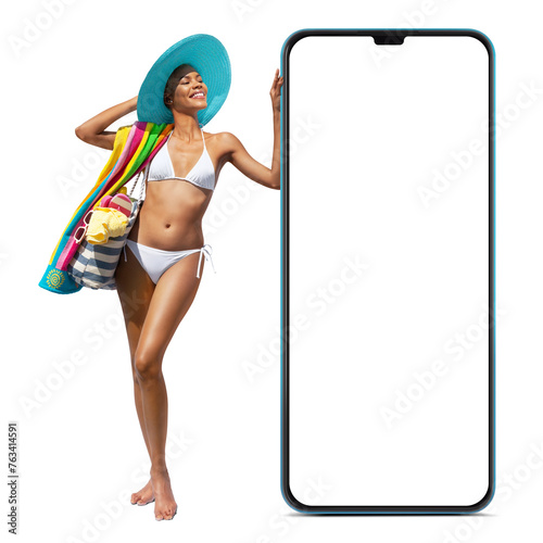 Happy girl in summer beach holiday wearing bikini and sun hat hold beach bag and towel, showing a big screen mobile phone isolated in white background, online shopping or booking sea vacation travels