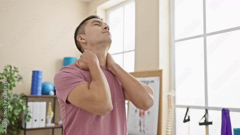 Smiling young man stretching neck in bright rehabilitation clinic room ...