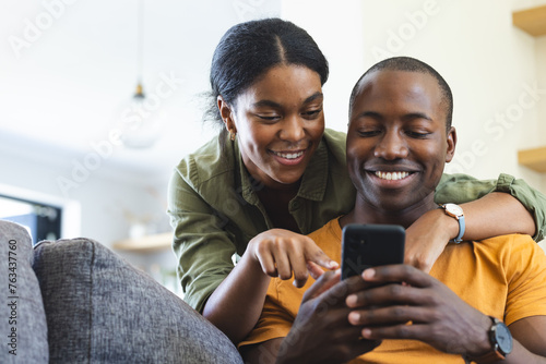 A diverse couple is using a smartphone on the couch at home