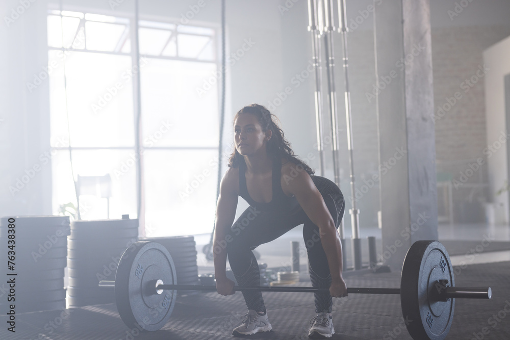 A fit Caucasian woman is performing a deadlift with a barbell in a gym A fit Caucasian woman is performing a deadlift with a barbell in a gym