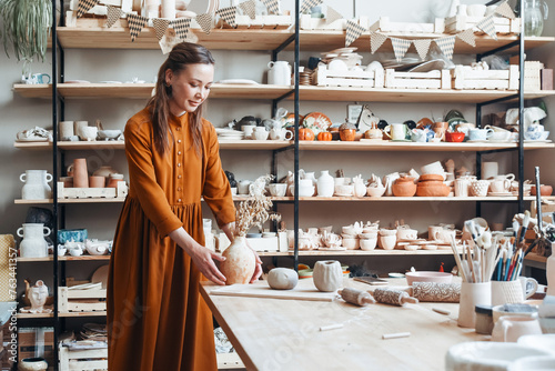 Handmade Craft: Woman with Earthenware in Pottery Shop. Young brunette potter with a serene expression showcasing her handmade vase in a pottery shop