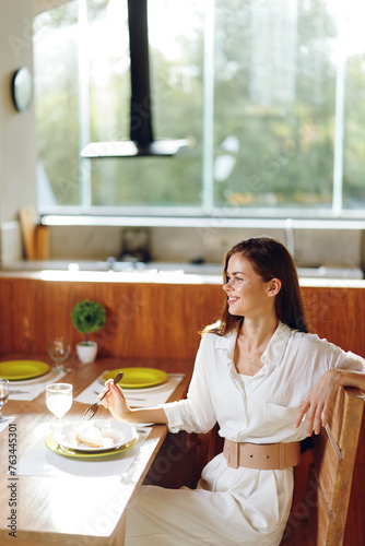 Smiling Woman Enjoying a Romantic Dinner at Home with a Stylish Table Setting A beautiful brunette woman sits at a trendy dining table  surrounded by elegant decorations and a delicious homemade meal