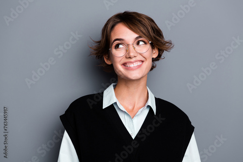 Photo of positive dreamy lady entrepreneur dressed black vest eyewear looking empty space isolated grey color background