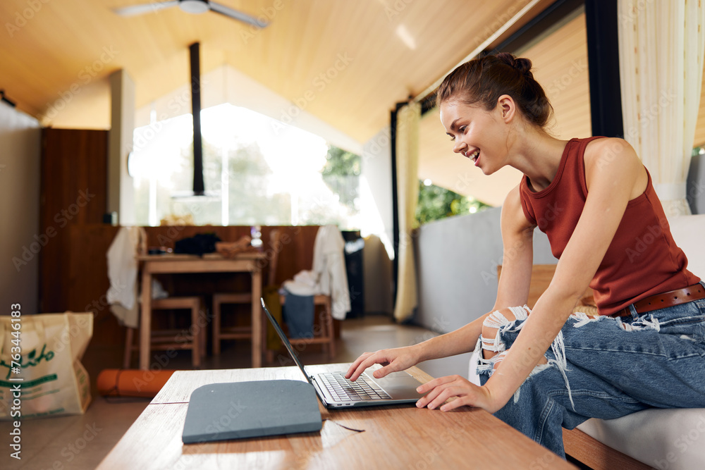 Obraz premium Smiling Woman Relaxing on Sofa with Laptop in Home Office, Enjoying Online Education and Working in Comfortable Living Room or Young Woman Sitting on Couch, Using Laptop with Joyful Smile, Creating a