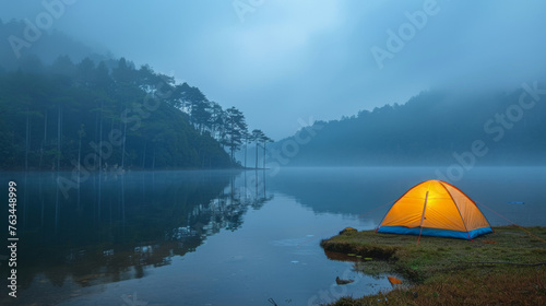 Illuminated tent at lakeside campsite. Foggy early morning. Outdoor adventures. Camping. Traveling.