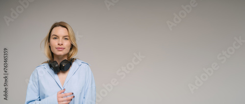 Music lover blonde woman in blue shirt with black headphones looking at the camera. Gray background. Long horizontal banner copy empty space