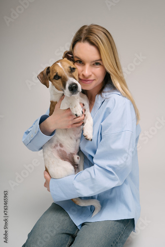 Woman hugging dog portrait. Adorable friends studio portrait. Blonde girl holding her pet Jack Russell terrier, sitting on the floor in photo studio