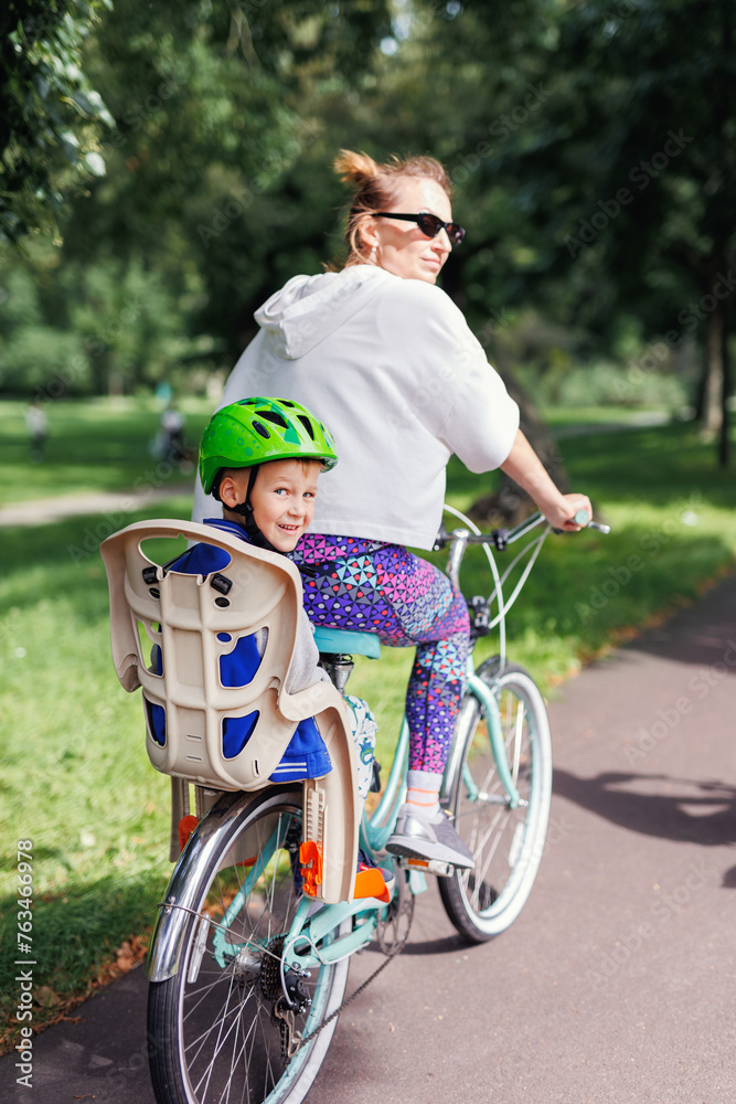 Smiling happy family enjoy riding bikes at Europe city streets on bright sunny day. Mom with children cycling at town park. Kid seating in safety baby chair bicycle. Healthy lifestyle activities Smiling happy family enjoy riding bikes at Europe city streets on bright sunny day. Mom with children cycling at town park. Kid seating in safety baby chair bicycle. Healthy lifestyle activities
