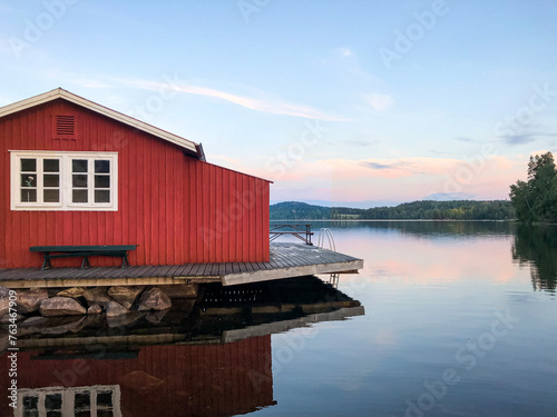 Rotes Holzhaus am See mit Steg, Blick über den See bei Sonnenuntergang