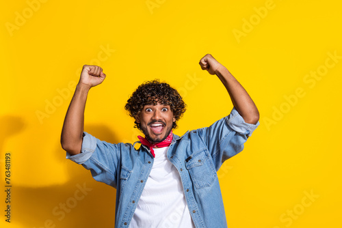 Photo portrait of attractive young man raise fists scream yes wear trendy denim clothes red scarf isolated on yellow color background