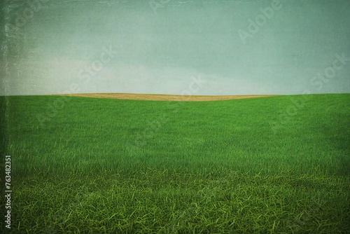 Green grass field and blue sky with grunge textured paper background