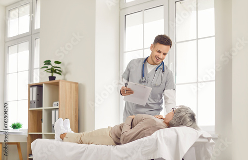 Senior woman patient lies on a couch and talking  consults with a young smiling doctor or nurse in a hospital office. Positive conversation about healthcare in medical clinic environment.