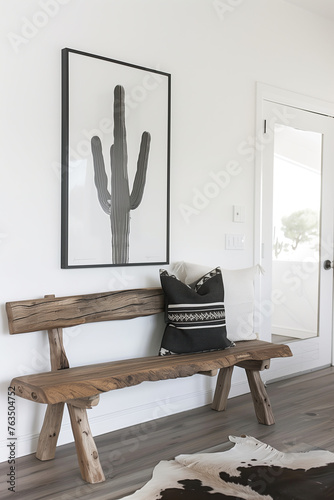 A rustic wooden bench with black and white cushion against the wall in modern farmhouse style home entryway, above it is hanging cactus artwork frame print on the wall, cowhide rug, white walls photo
