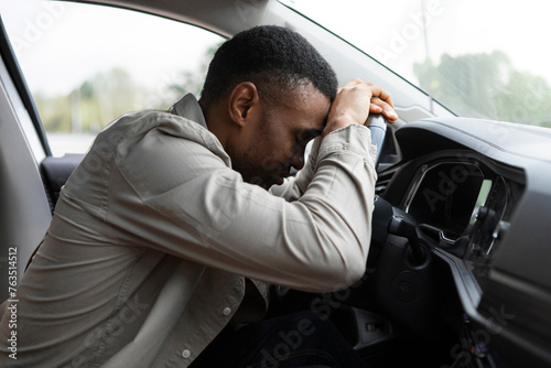 African american man sleeping in a car, resting head on wheel