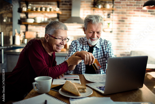 Smiling senior couple using credit card on laptop at home